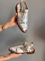 Sandalias plateadas de cuero con diseño tipo pescador, suela plana y hebilla lateral.