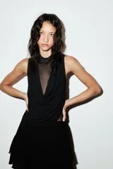 Falda pantalón negra de tiro bajo con cintura drapeada y bajo acabado en volantes superpuestos. Presenta un lazo largo y fino que cae desde el lateral.