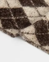 Bufanda tejida bicolor con terminación de borlas y tag de goma. Diseño de rombos en tonos marrón y beige.