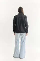 Camisa color crema con cuello clásico, cierre frontal con botones y mangas largas. Presenta detalles de bordado calado en el frente y los puños.