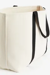 Bolso de playa de lona color crudo con asas de cinta negra.