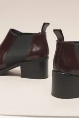 Botín negro de cuero vacuno con acabado charol, estilo botín Chelsea con puntera fina y elástico lateral. Posee un taco ancho y bajo de 5.5 cm.