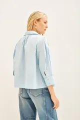 Camisa celeste de poplin con bordados de palmeras doradas en el frente, de corte amplio, con cuello y cartera.
