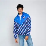 Campera deportiva Umbro Windbreaker del Club Nacional de Football. Diseño con paneles en azul y estampado geométrico en azul, rojo y blanco. Incluye capucha, cierre frontal y logo de Umbro y escudo del club en el pecho.