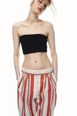 Pantalón de tiro medio con estampado de rayas verticales negras sobre fondo blanco. Tiene trabillas en la cintura, bolsillos laterales, pinzas delanteras y cierre frontal con cremallera, botón y ganchos metálicos.
