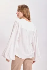 Blusa blanca de mangas largas abullonadas con cuello en V y detalle de botón en el frente.