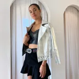 Chaqueta de cuero negra con cuello clásico, cierre frontal asimétrico con cremallera, solapas con muescas y detalles de tachas plateadas en los hombros y puños.