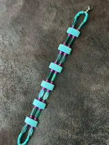Gargantilla corta con cuentas de piedra color turquesa, ojos de tigre color marrón, resina color verde y cristales facetados color rosa. Se cierra con cadena de acero quirúrgico y ganchito para ajustar.