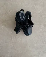 Zuecos negros de cuero con hebilla y tachas decorativas.