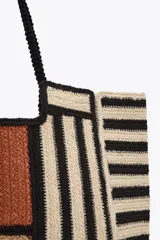 Bolso tipo tote de yute con diseño de bloques de color y rayas horizontales en negro y beige. Asas de hombro negras.
