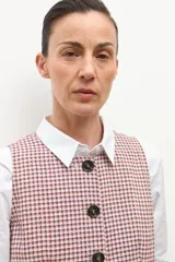 Chaleco de vestir sin mangas, color beige con estampado de cuadros pequeños en tonos rojizos y marrones. Tiene cuello solapa y cierre frontal con botones oscuros.