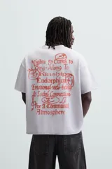 Sudadera lila de corte holgado con cuello redondo y manga corta. Presenta textos estampados en color rojo en el frente y la espalda. Tiene efecto lavado y acabados irregulares.
