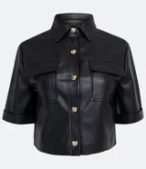 Camisa de manga corta confeccionada en material sintético color beige. Tiene cuello camisero, cierre de botones en forma de corazón, dos bolsillos con solapa y corte cropped.