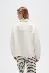 Campera de jean color crudo, de corte recto, con cuello clásico, cierre frontal con botones metálicos, dos bolsillos con solapa en el pecho y bajo con detalle de bordado calado.