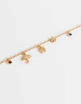 Pulsera dorada de cadena fina con dijes colgantes de corona, taza de té, oso de peluche y cristal azul.