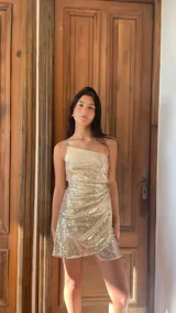 Vestido corto dorado con lentejuelas, de un solo hombro, con breteles finos y falda irregular con capas y frunces.