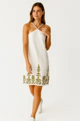 Vestido blanco de lino y algodón, con cuello halter, tiras finas cruzadas en la espalda y bordado floral en el ruedo.