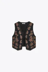 Chaleco negro de efecto ante con bordados florales color cobre y tachas doradas. Tiene escote en pico, sisas amplias y cierre frontal con lazos.