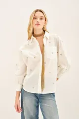 Camisa blanca de algodón con bordado de corazones dorados, corte amplio, cuello clásico, cartera con botones ocultos y bolsillo en el pecho.