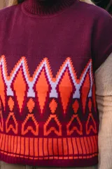 Chaleco de punto color borgoña con cuello alto y diseño geométrico en naranja y blanco.