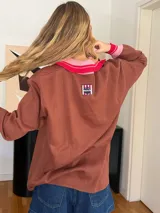 Buzo marrón de algodón con cuello polo rosa y puños acanalados rosas con rayas rojas.