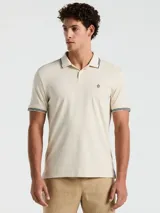 Polo color crema con cuello clásico, mangas cortas y logo bordado en el pecho. Presenta detalles de doble línea en cuello y mangas.