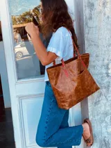 Bolso tote de cuero color marrón con asas trenzadas en marrón y rojo.