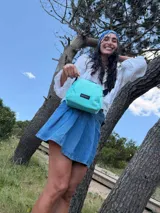 Bandolera pequeña de tela negra, con correa ancha ajustable y cierre superior.