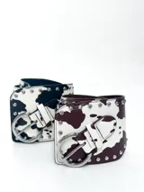 Cinto faja ancho con estampado de vaca en blanco y negro, con hebilla metálica plateada y tachas decorativas.