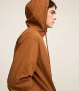 Campera rompevientos color verde oliva, con capucha ajustable con cordón, cierre frontal con cremallera, bolsillos laterales con cremallera y puños elásticos.
