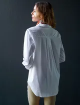 Camisa blanca de manga larga, corte holgado, con cuello con solapa, abertura central con botones y bolsillo aplicado en el pecho.