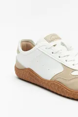 Zapatillas de cuero color blanco y beige, de diseño minimalista con suela marrón.