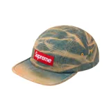 Gorro de cinco paneles Supreme, confeccionado en denim con diseño tie-dye en tonos celeste y amarillo. Presenta el logo de Supreme en color rojo en el panel frontal.