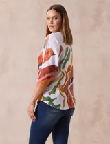 Buzo blanco con estampado abstracto en tonos naranja, verde, marrón y rojo. Tiene cuello redondo y mangas 3/4.
