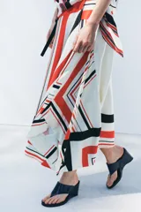 Falda midi de tiro medio con estampado de rayas rojas, negras y blancas. Tiene bajo asimétrico y cierre frontal tipo pareo ajustable con lazos negros.