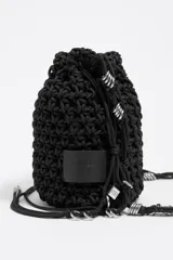 Bolso tipo bucket negro tejido con cordones, con etiqueta de cuero con logo Bimba y Lola y charms metálicos plateados.