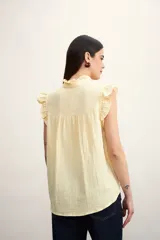 Camisa color amarillo pálido con cuello mao, sin mangas, con volados en los hombros y en el frente.