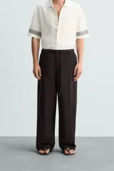 Pantalón marrón oscuro de corte amplio, confeccionado en mezcla de algodón y lino. Presenta cintura elástica, bolsillos laterales y trasero de parche, pliegues frontales, cierre con cremallera y botón.