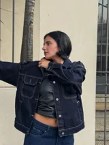 Campera de jean azul oscuro con costuras en hilo ocre, corte recto, cuello clásico, bolsillos frontales con solapa y cierre con botones metálicos.