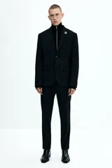 Blazer negro de corte slim fit, con solapas de muesca finas y ojal decorativo. Modelo de botonadura sencilla con bolsillo superior insertado, bolsillos delanteros con solapa, dos bolsillos en el interior y botones decorativos en los puños. Abertura doble atrás.
