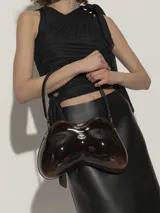 Bolso de hombro Diesel con forma orgánica y curvilínea, similar a un control de videojuegos. Acabado brillante, color negro con efecto degradado a gris oscuro en la parte inferior. Cuenta con un asa de hombro fina y un pequeño dije metálico con logo en el centro.