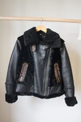 Campera gamulán marrón con interior de piel sintética blanca, cierre frontal con cremallera, cuello con solapas y dos bolsillos con cierre.