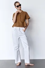 Chaqueta color marrón de tejido de punto, con cuello solapa, manga corta y bajo evasé con volantes. Cierre frontal con botones forrados a tono.