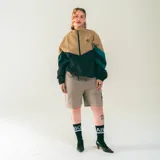 Campera deportiva unisex color beige, negro y verde azulado, confeccionada en nylon liviano con calce relajado y estructura clásica. Incluye paneles diagonales en contraste, cierre frontal y micrográfico Kaboa aplicado al frente y un gráfico en la espalda.