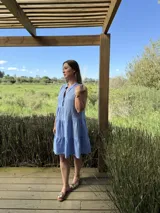 Vestido verde militar de lino, corte a la rodilla, sin mangas, con cuello mao y botones de nácar. Presenta varios cortes en su largo, aportando movimiento y un toque moderno a este diseño fresco y elegante.