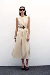 Vestido midi color beige, de popelín, con cuello redondo y sin mangas. Presenta cintura entallada con pinzas, cinturón y falda evasé.
