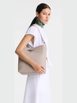Bolso tipo hobo de cuero color negro, con asa de hombro ajustable y cierre superior con broche metálico.