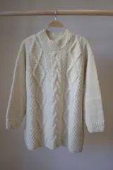 Sweater tejido a mano en lana merino color crudo, con cuello redondo y diseño de trenzas en el frente.