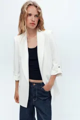 Blazer blanco con cuello solapa y hombreras. Manga por debajo del codo acabada en vuelta con trabilla y botón dorado. Bolsillos delanteros con solapa.