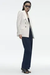 Blazer color blanco hueso, de corte entallado y doble botonadura dorada.